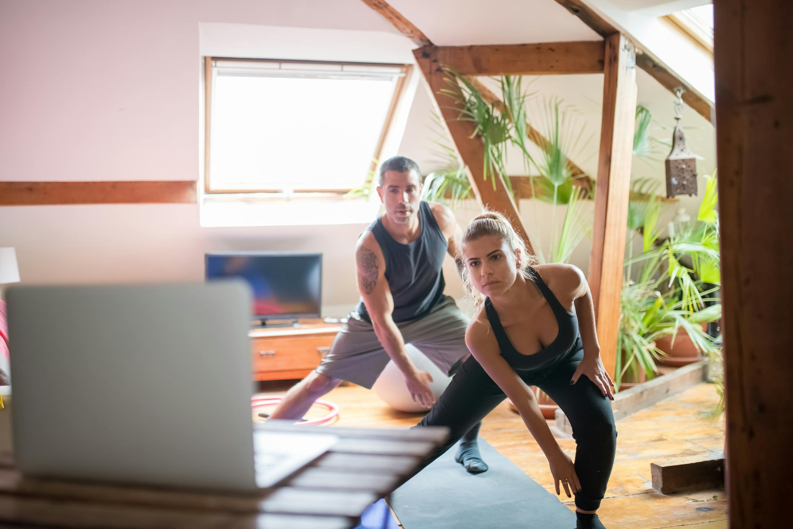 A man and woman working out at home using a laptop for guided exercises. Indoor active lifestyle.