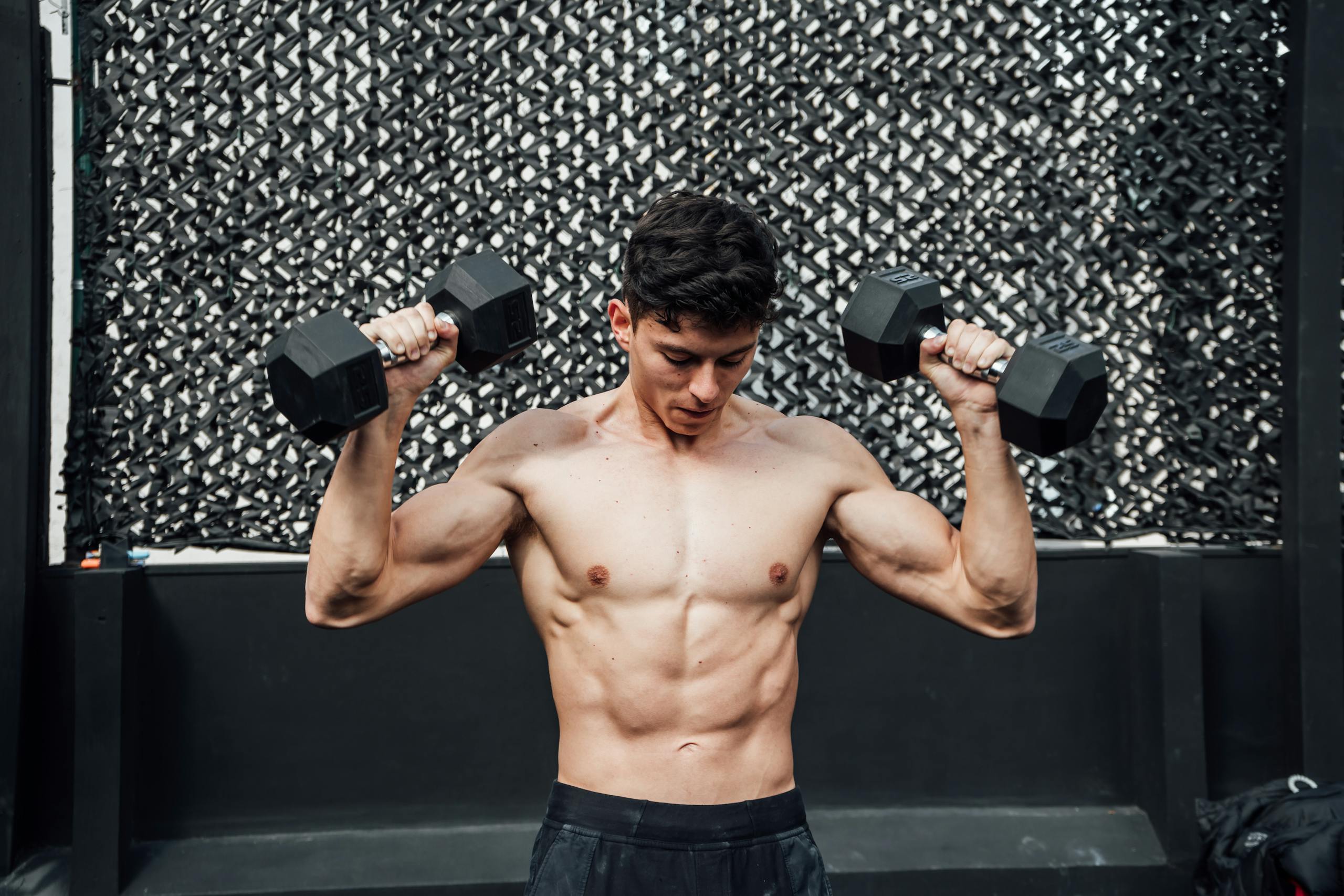 A shirtless muscular man lifts dumbbells at a gym in Mexico City.